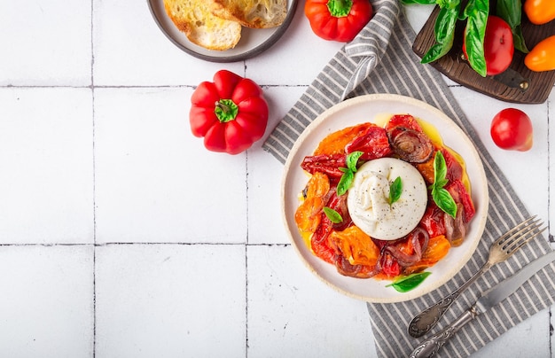 Burrata-kaas met gebakken tomaten, peper, rode ui en vers basilicum op witte tegelachtergrond