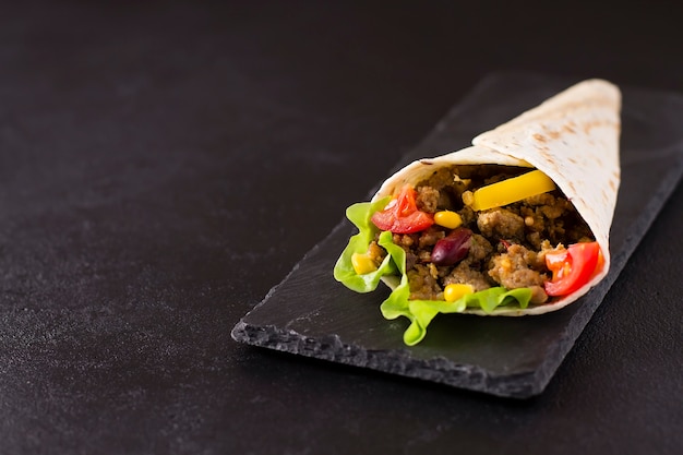 Burrito with beef, chicken, lime, pepper and vegetables, on a stone board. Grey background. Mexican food.