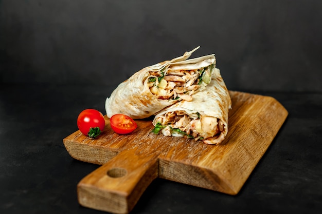 Il burrito si avvolge con pollo e verdure su un tagliere, su uno sfondo di cemento, shawarma messicano