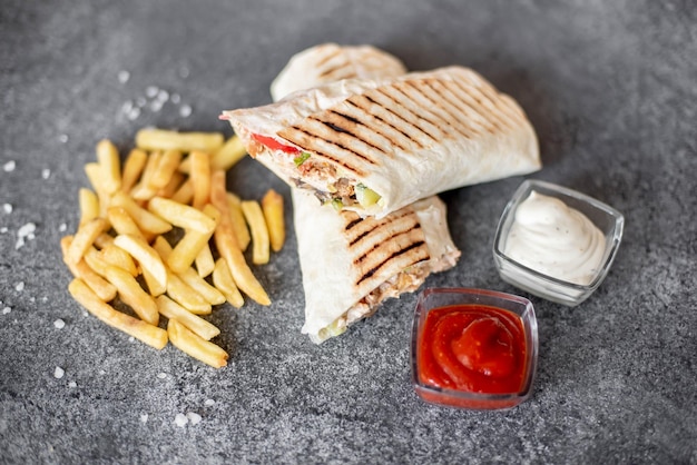 Burrito wraps with chicken and vegetables and french fries on stone background