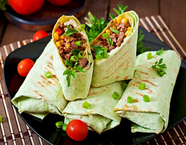 Burritos wraps with minced beef and vegetables on a wooden surface