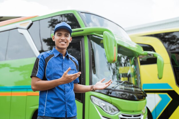 A bus driver in a uniform and a hat with a hand gesture presents something  against the bus
