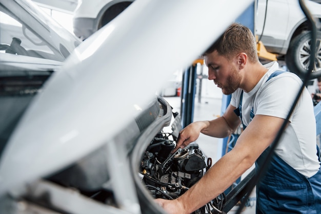 Bus repareert. Werknemer in het blauw gekleurde uniform werkt in de autosalon