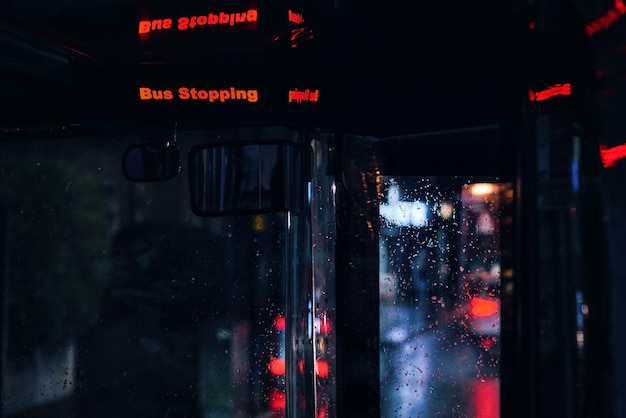 Bus stopbord knipperend in het openbaar vervoer op regenachtige avond, wazige weg en lichten achtergrond.