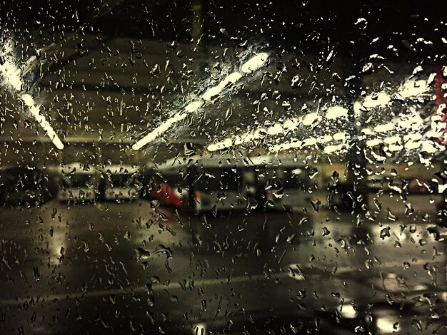 Photo buses in illuminated parking lot seen from wet glass window