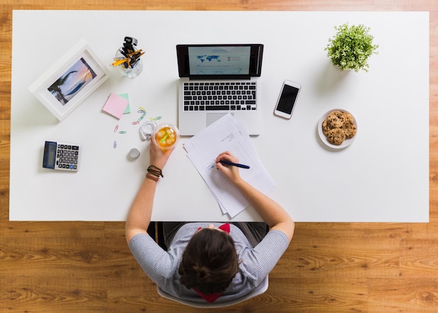 business accounting and freelance concept woman with papers cup of drink and laptop computer working at office table