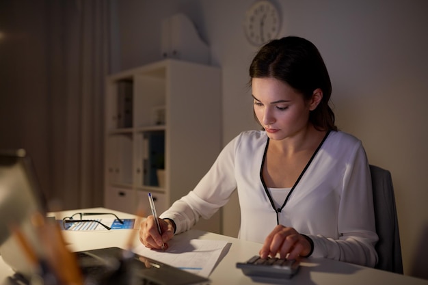 business, accounting, overwork, deadline and people concept - woman with tax form and calculator working at night office