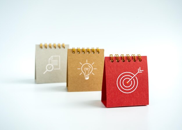 目標のアイデアと研究のアイコンを含むビジネスアクションプランは、白い背景に小さな赤いベージュとグレーのデスクカレンダー2023年に署名し、戦略コンセプトの最小限のスタイルの3つのステップ