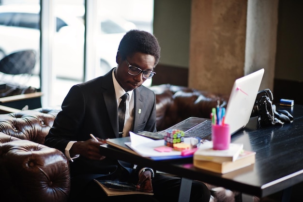 Business african american man wear on black suit and glasses sitting at office with laptop and working