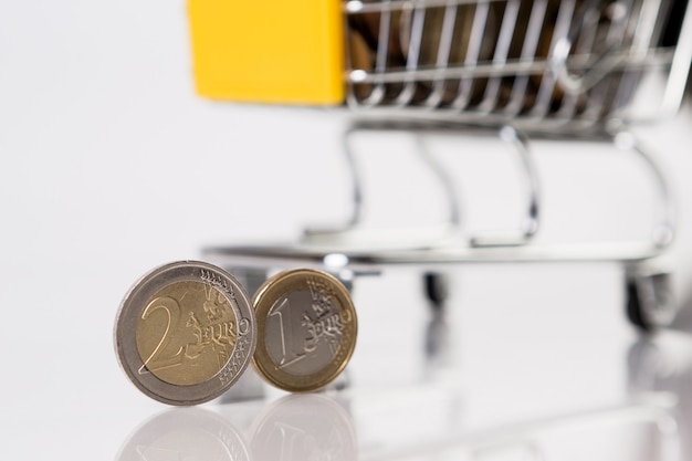 Фото Бизнес и финансы, концепция покупок с тележкой для покупок с несколькими монетами на белом фоне