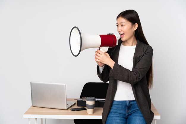 Photo business asian woman in her workplace isolated on white space shouting through a megaphone