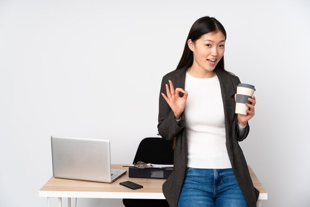 손가락으로 확인 표시를 보여주는 흰 벽에 그녀의 직장에서 비즈니스 아시아 여자