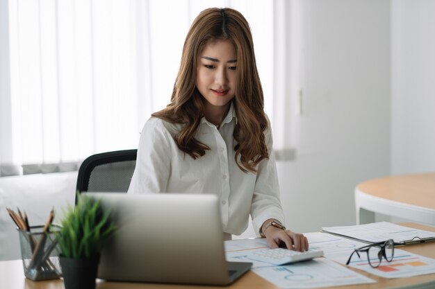 Photo business asian woman using calculator at working with financial report. she working with laptop computer.