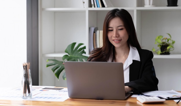 Business asian woman using laptop for do math finance on wooden desk in office, tax, accounting, financial concept