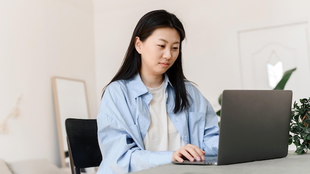 Деловая азиатка, работающая на ноутбуке дома Владелец малого бизнеса или фрилансер проходит обучение в домашней обстановке