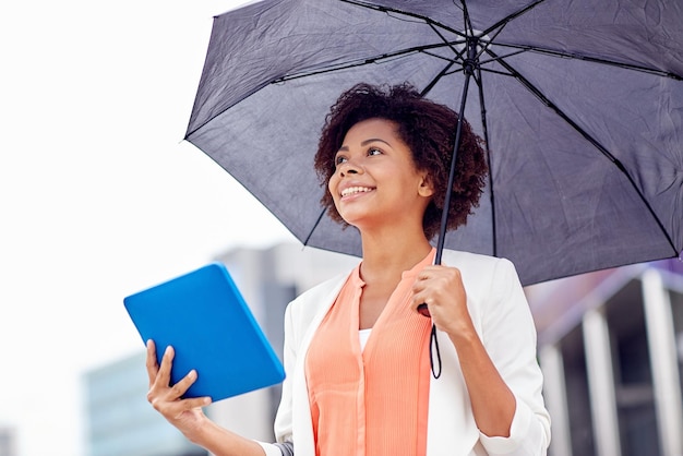 business, bad weather and people and concept - happy african american businesswoman with umbrella and tablet pc computer at city street