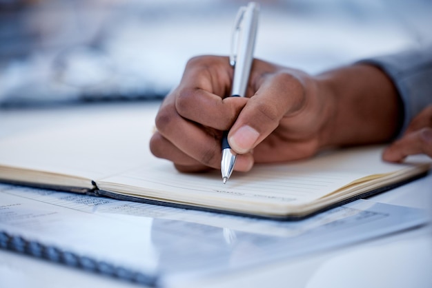 Business black man and hands writing in notebook diary and strategy ideas Closeup worker planning with pen notes and schedule of information in journal reports or logistics agenda at office desk