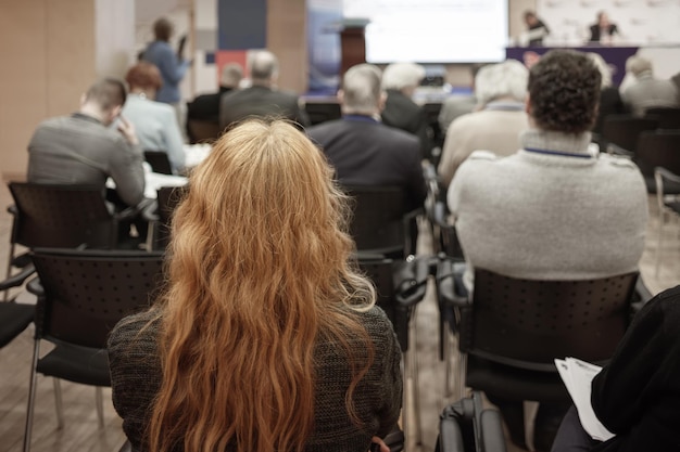Фото Деловая блондинка с длинными волосами и людьми, слушающими конференцию или тренировку в зале