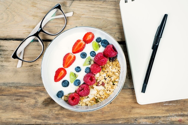 Photo business breakfast with a bowl of yogurt with notepad and glasses on the wooden table