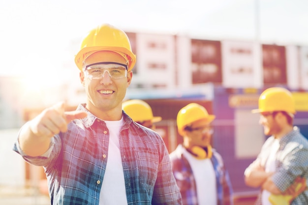 business, building, construction, gesture and people concept - group of smiling builders in hardhats pointing finger on you outdoors