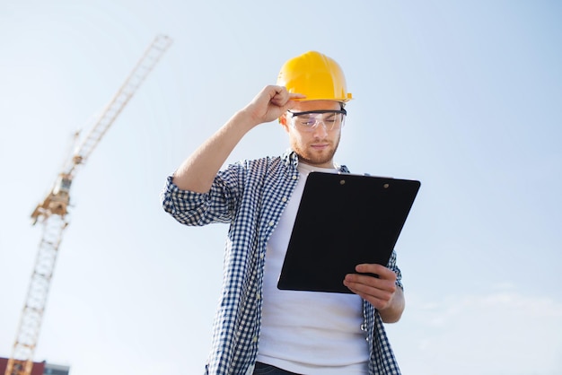 business, building, paperwork and people concept - builder in hardhat with clipboard outdoors