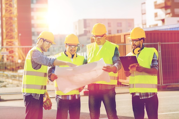 business, building, teamwork, construction and people concept - group of smiling builders in hardhats with blueprint and clipboard