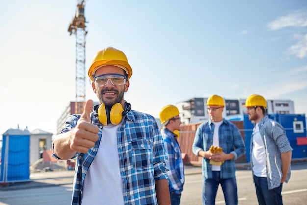 비즈니스, 건물, 팀워크, 제스처 및 사람 개념 - 건설 현장에서 엄지손가락을 보여주는 안전모를 쓴 웃는 건축업자 그룹