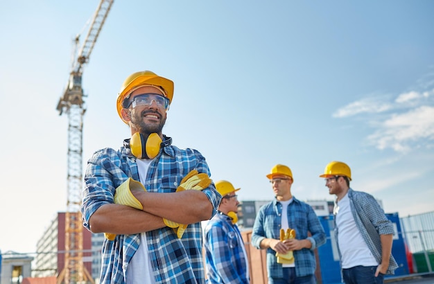 Concetto di affari, costruzione, lavoro di squadra e persone - gruppo di costruttori sorridenti in elmetti protettivi in cantiere