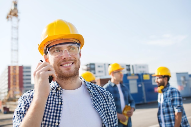 business, building, teamwork, technology and people concept - group of smiling builders in hardhats with radio outdoors