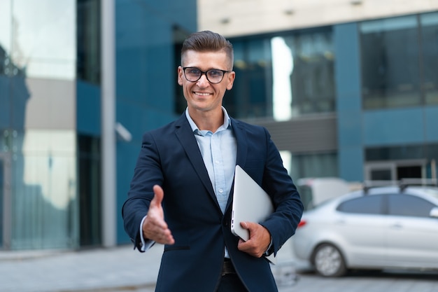 Business. Businessman Giving Hand For Handshake Welcome Gesture Adult Caucasian Male Business Person Holding Closed Laptop Give Hand Ready Handshake Office Building Background