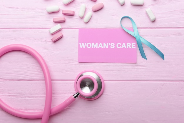 Business card with text womans care ribbon and pills on pink wooden background