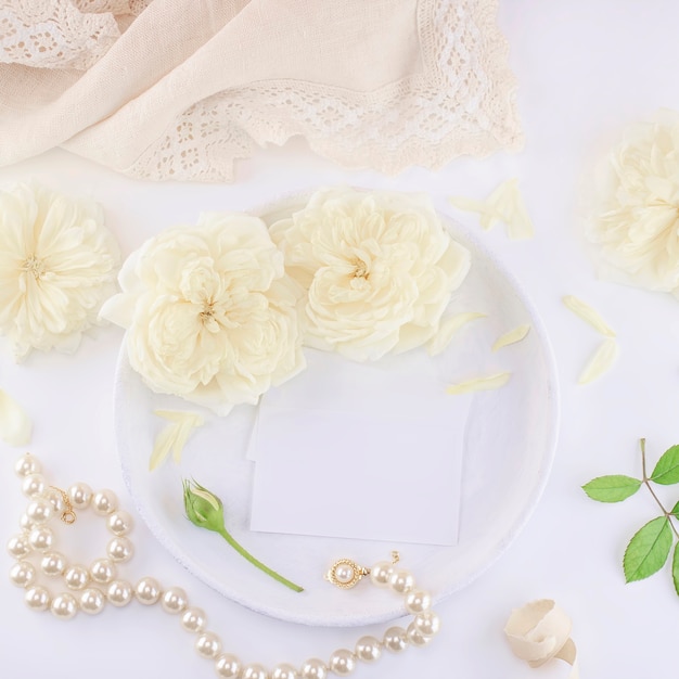 Business cards mockup on a white plate with roses and pearl necklace.