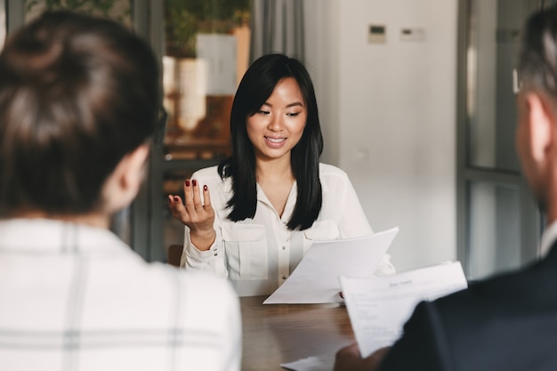 Photo business, career and placement concept - businesslike asian woman holding resume and speaking to employers of big company, during corporate meeting or job interview