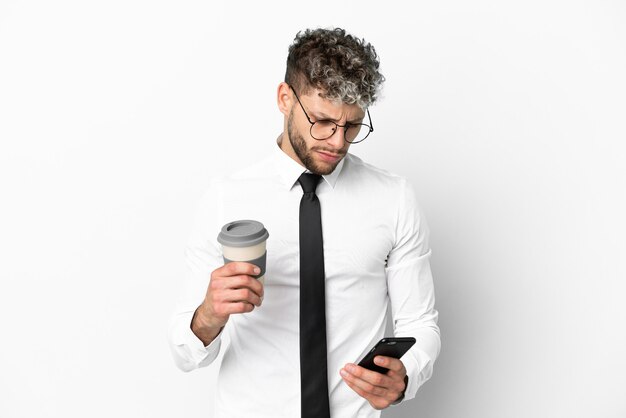 Business caucasian man isolated on white background holding coffee to take away and a mobile