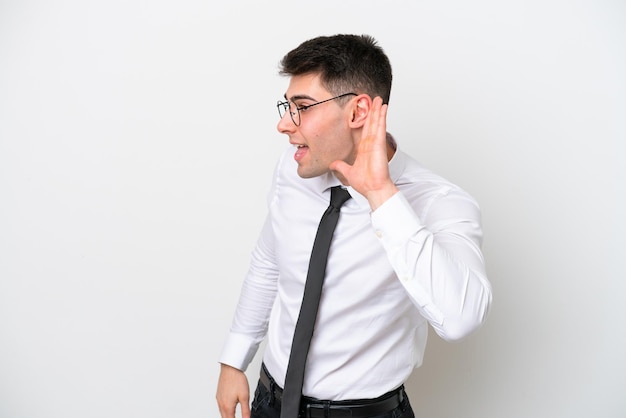 Business caucasian man isolated on white background listening to something by putting hand on the ear