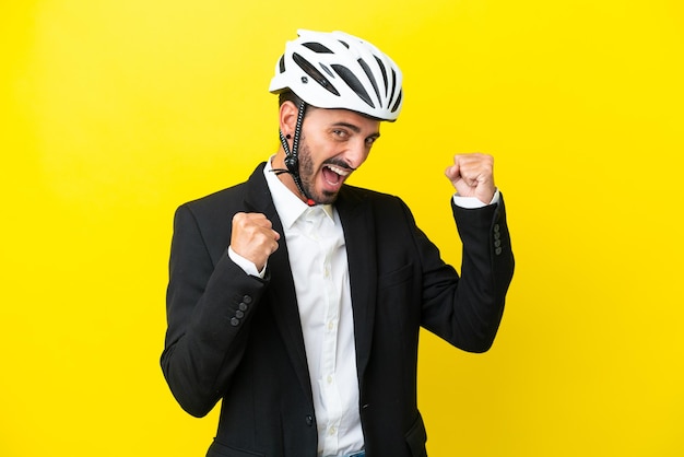 Business caucasian man with a bike helmet isolated on yellow background celebrating a victory