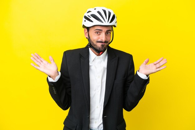 Business caucasian man with a bike helmet isolated on yellow background having doubts while raising hands