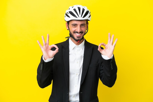 Деловой кавказец в велосипедном шлеме на желтом фоне показывает пальцами знак "ок"
