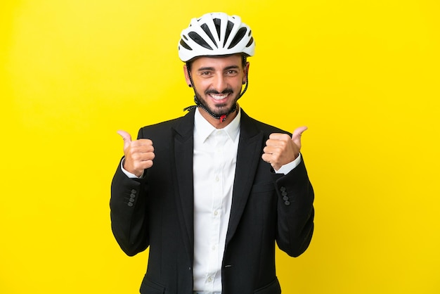 Uomo caucasico d'affari con un casco da bici isolato su sfondo giallo con il pollice in alto gesto e sorridente