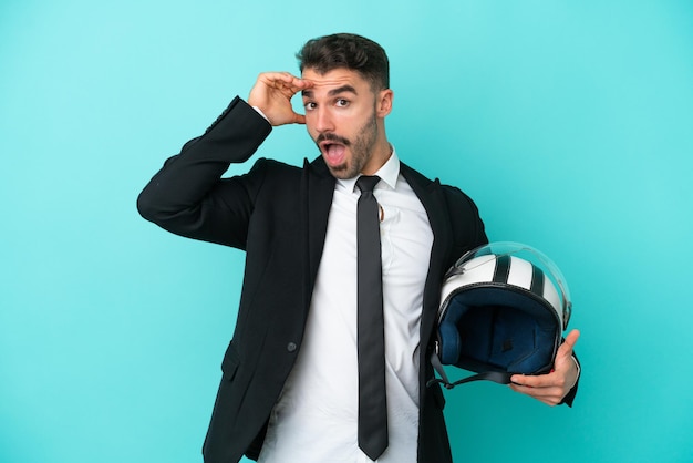 Business caucasian man with motorbike helmet isolated on blue background doing surprise gesture while looking to the side