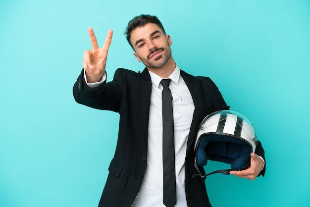 Business caucasian man with motorbike helmet isolated on blue background smiling and showing victory sign