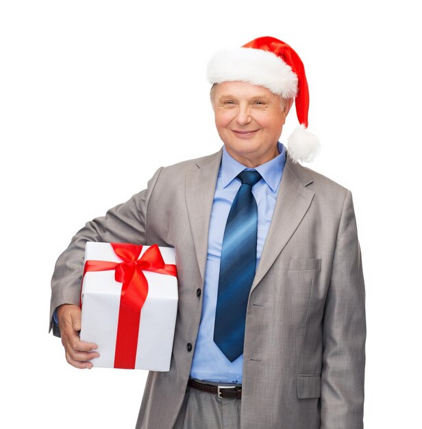 business, christmas, xmas, happiness concept - smiling old man in suit and santa helper hat with gift