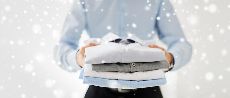 Photo business, clothing and people concept - close up of businessman holding folded shirts over snow effect
