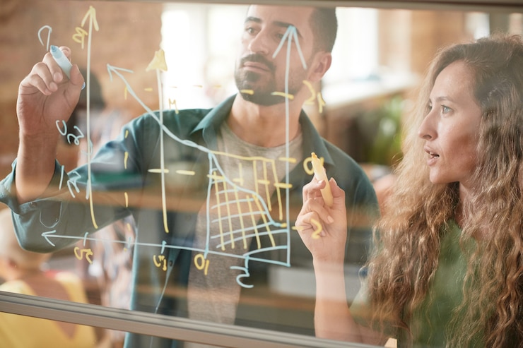 Photo business colleagues drawing financial graphic on glass wall and examining it together in team during presentation at office