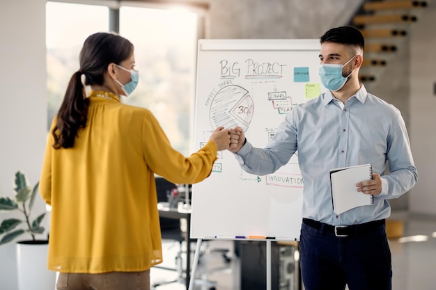 Business colleagues fist bumping while wearing protective face masks in the office