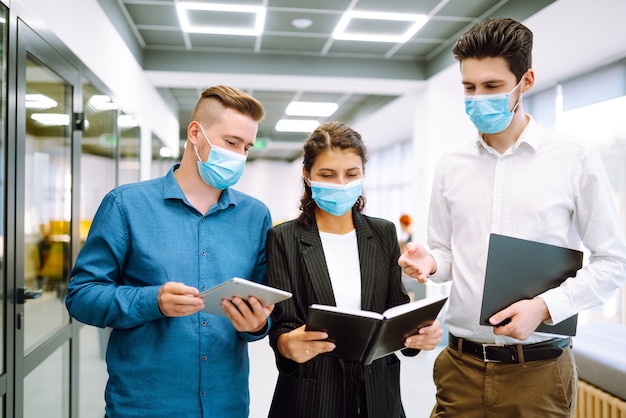 Business colleagues in protective face masks in modern office discussing together work issues.