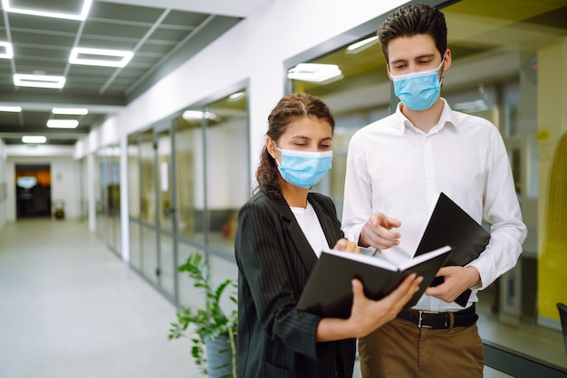 Business colleagues wearing medical face mask discussing together work issues at office. Teamwork during pandemic in quarantine city. Covid-19.