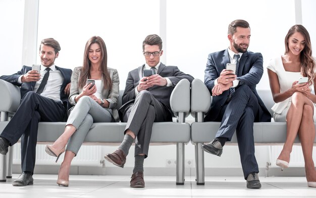 Business colleagues with their smartphones sitting in the office hallway