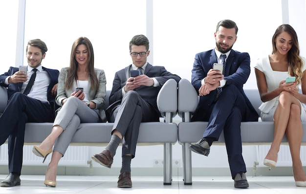 Коллеги по бизнесу со своими смартфонами сидят в коридоре офиса, люди и технологии