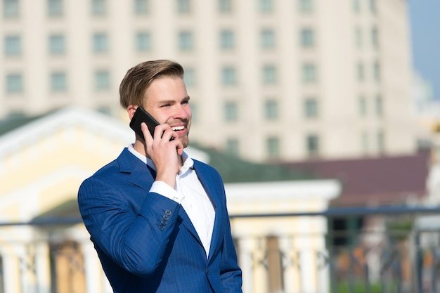 Business communication and new technology Happy businessman with smartphone on sunny terrace Man smile in formal suit with mobile phone outdoor Business lifestyle concept